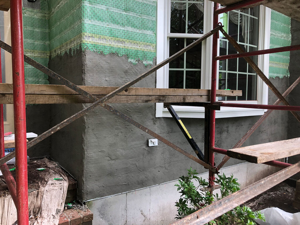 Exterior walls prepared with reinforcing mesh and a mortar base coat before natural stone veneer installation