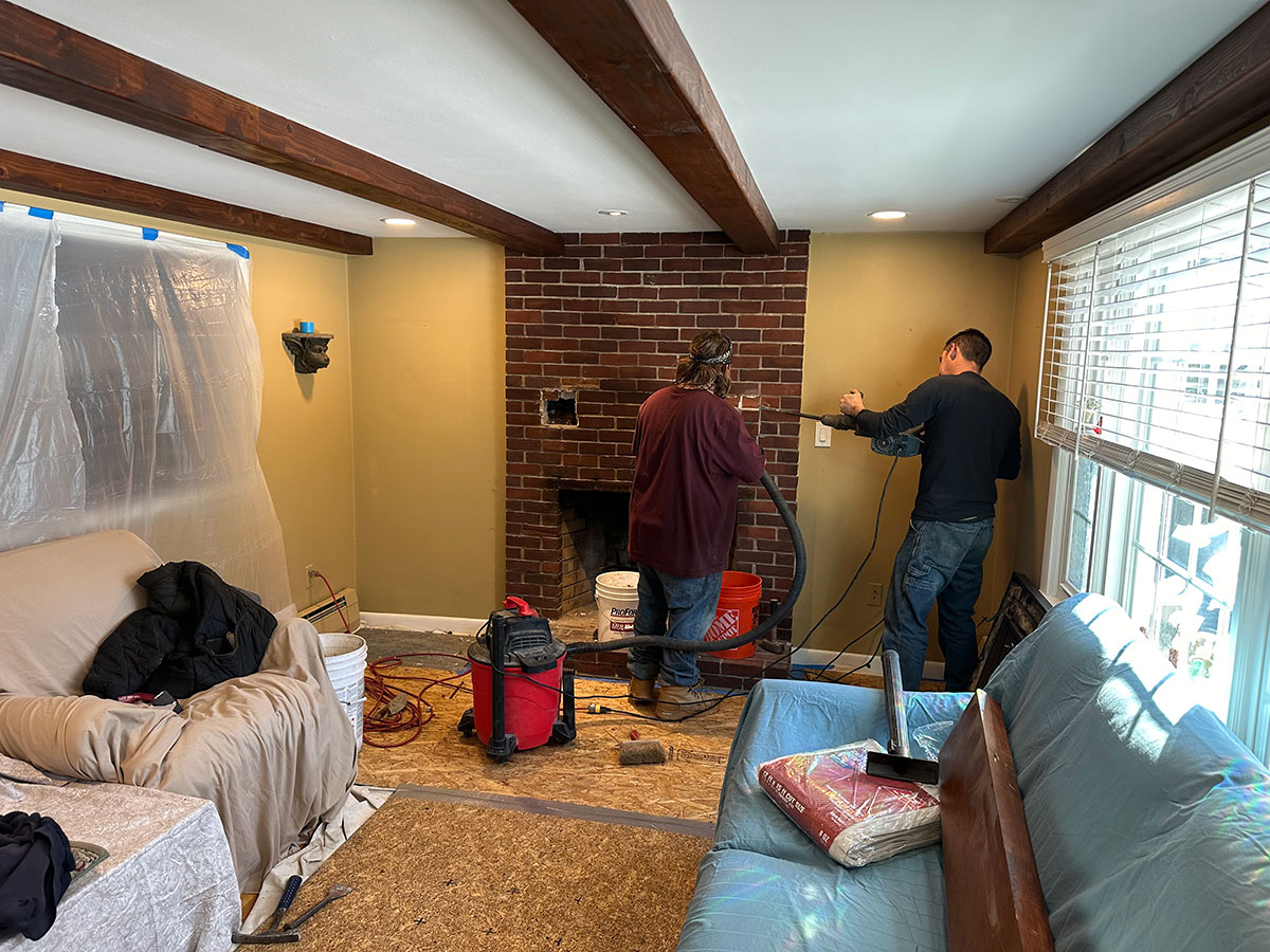 Masons removing part of the original brick fireplace while using a vacuum to control dust