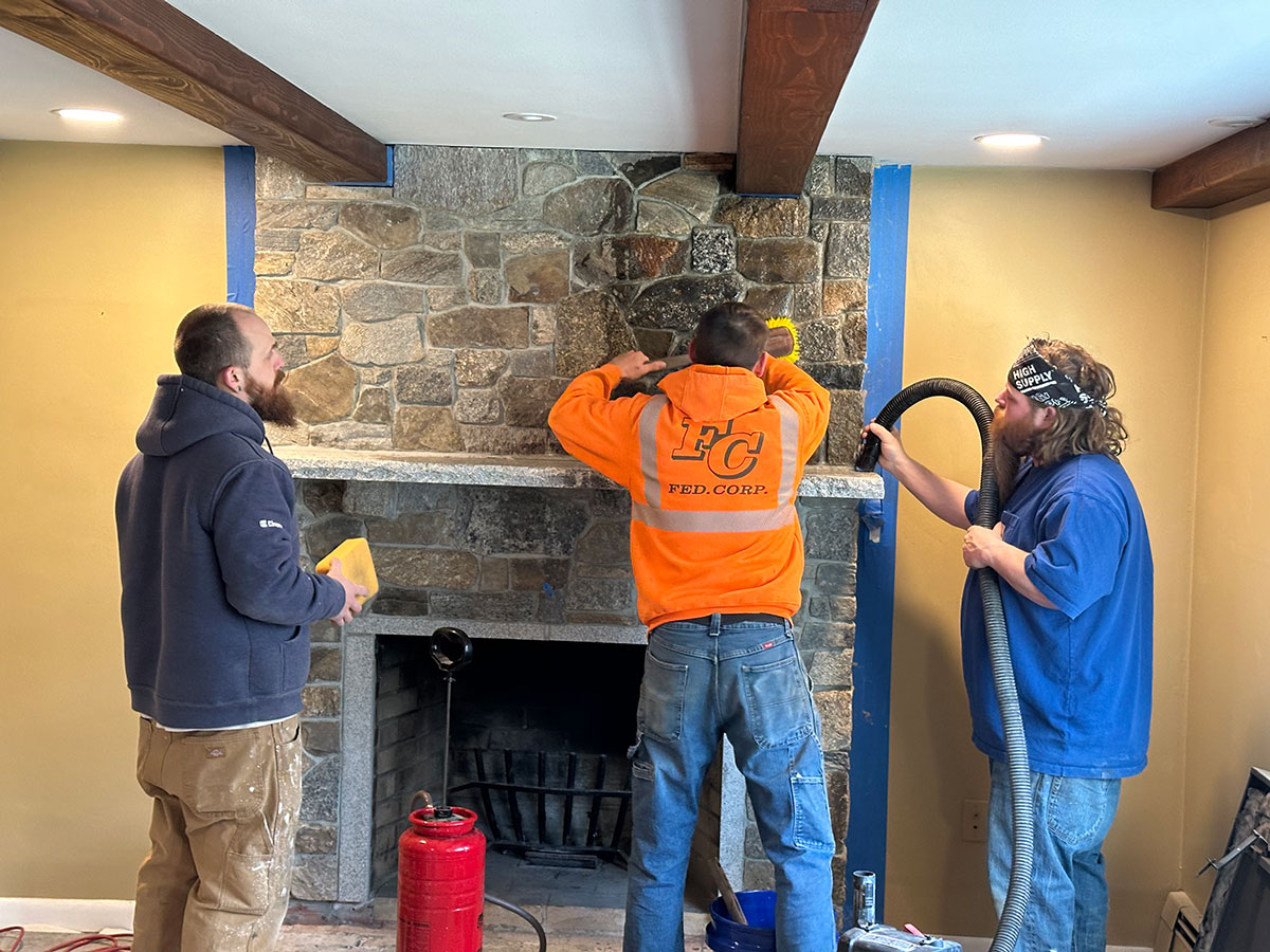 Crew cleaning and finishing the stone veneer around the granite mantel and fireplace opening