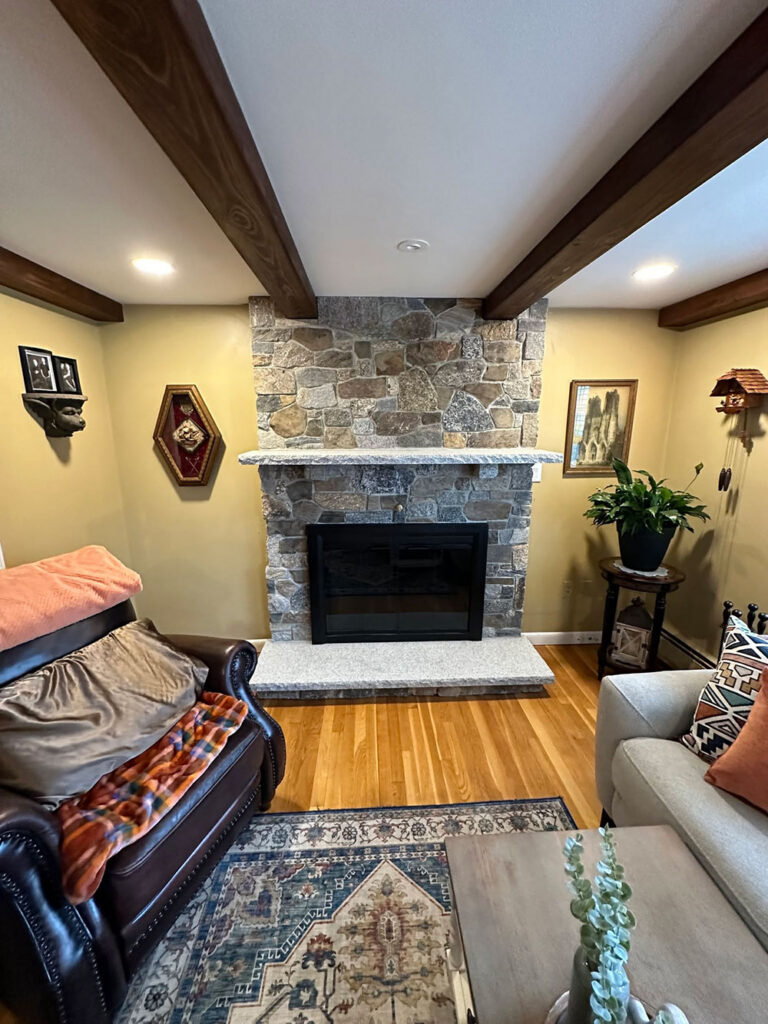 Completed stone veneer fireplace with granite mantel and hearth in a Raynham living room