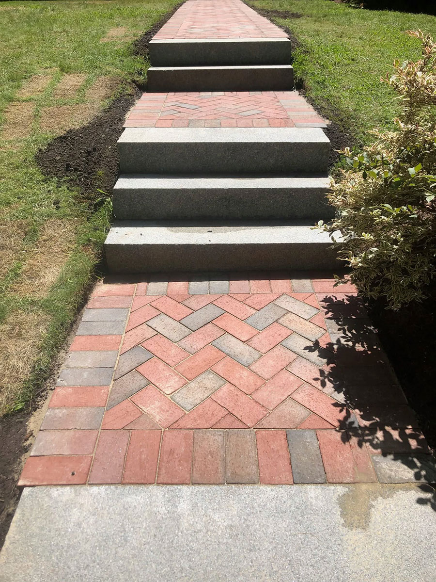 The completed walkway creates a continuous brick-and-granite approach across the sloping front yard.