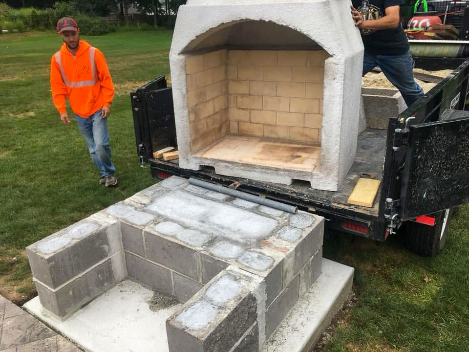 Yellow firebrick-lined outdoor fireplace core being installed on a masonry base