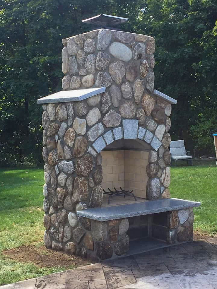 Completed natural stone outdoor fireplace with granite arch and raised hearth in Easton, MA