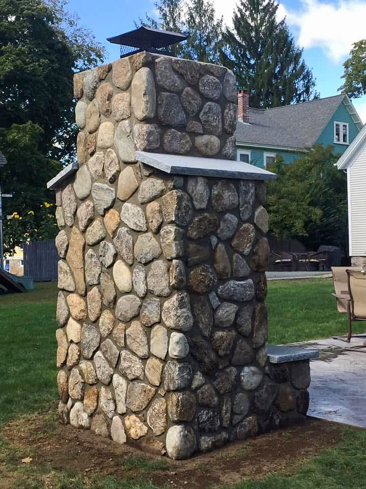 Side view of an outdoor fireplace with natural stone and granite shoulder caps