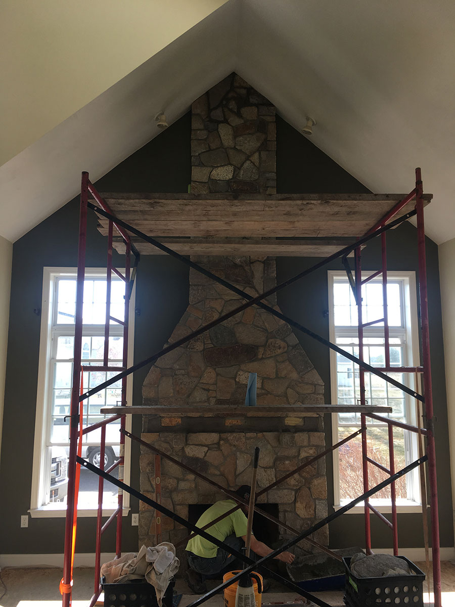 Floor-to-ceiling natural stone fireplace nearing completion beneath a vaulted ceiling