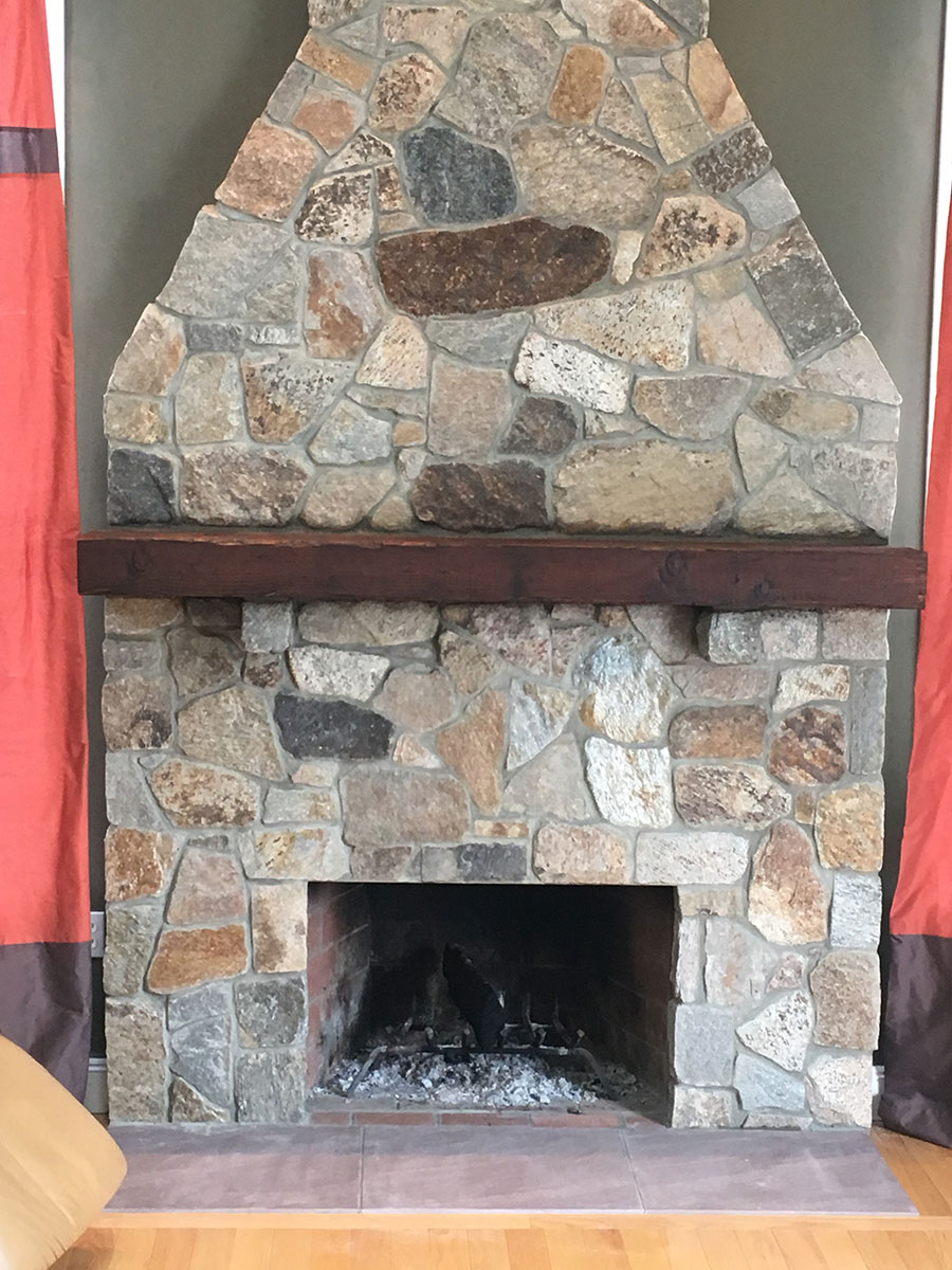 Close view of a completed Boston Blend Mosaic natural stone fireplace with a wood mantel in Stow, MA