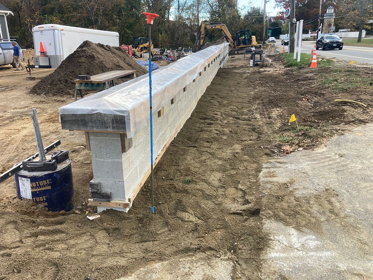 Long concrete block wall protected from weather before stone veneer and cap installation