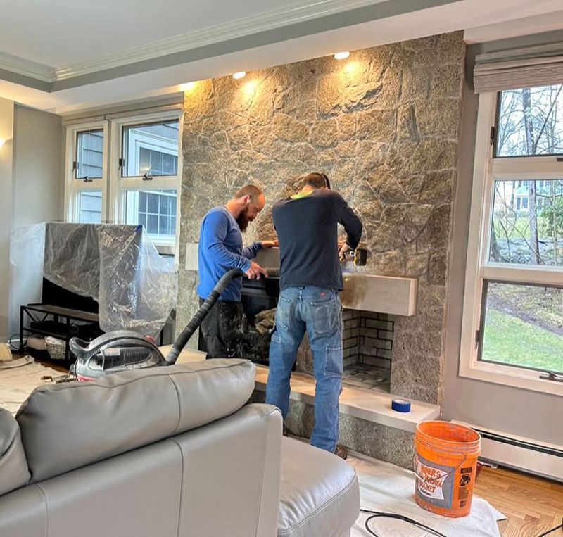 two masons repairing stone fireplace in residence